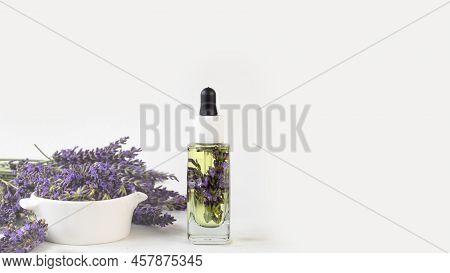 Glass Bottle Of Lavender Essential Oil With Fresh Lavender Flowers And Dried Lavender Seeds On White