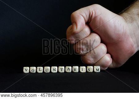 Inscription Voluntarism And A Clenched Male Fist On A Black Background. The Concept Of Voluntaristic