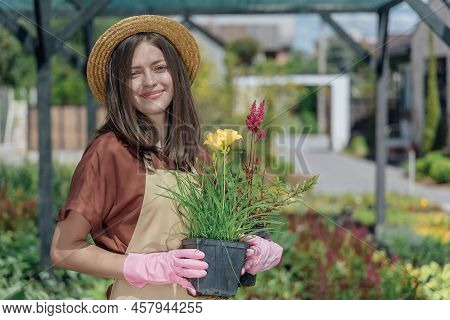 Portrait Of Woman-gardener Holding A Perrenial Plant In Hands And Working Near Garden House