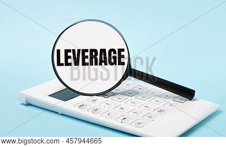 On A Blue Background, A White Calculator And A Magnifying Glass With The Text Leverage. Business Con