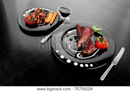 fresh red beef meat steak barbecue garnished vegetable salad sweet potato and basil on black plate over black wooden table with bbq sauce in sauce boat high resolution hidef