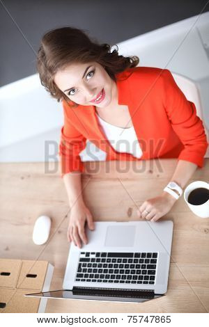 Attractive woman sitting at desk in office, working with laptop