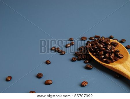 Arabica Coffee Beans in a Bamboo Spoon, Scattered Against a Blue Background