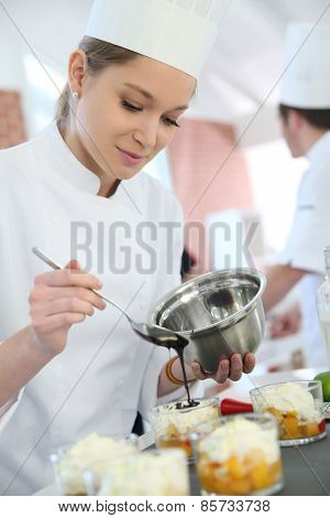Pastry cook student pouring chocolate sauce on dessert