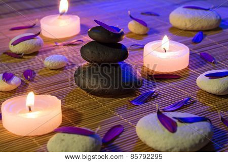 White and black stones, purple petals, and candles on bamboo