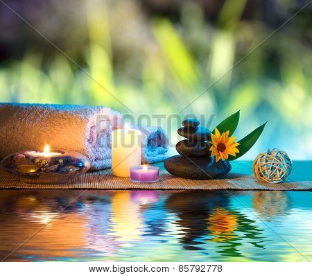 three candles and towels black stones and orange daisy on water