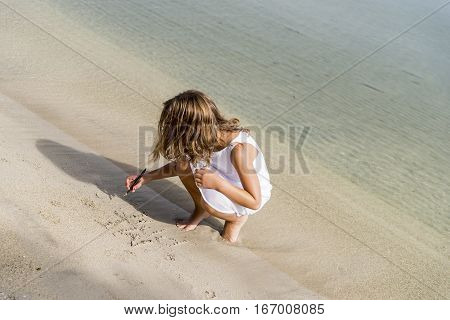 Little girl writing in the sand on the beach