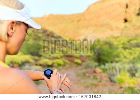 Woman runner checking the elevation on sports watch smartwatch with altimeter app in summer mountains. Young girl training and running on mountain trail in the morning.