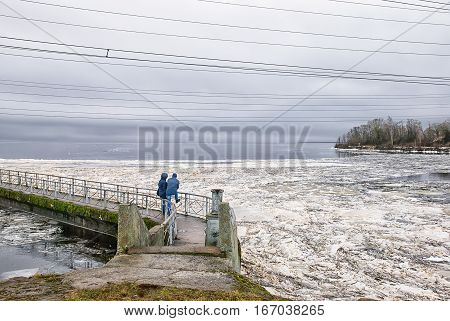 Ivangorod. Russia. Narva Reservoir. People standing on the icebreaking wall, and the pedestrian bridge on the wall opposite Estonia. Reservoir is located on the Russian-Estonian border