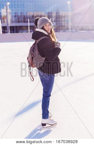 Young Woman With Bagpack Skates At Outdoor Skate Rink In Winter