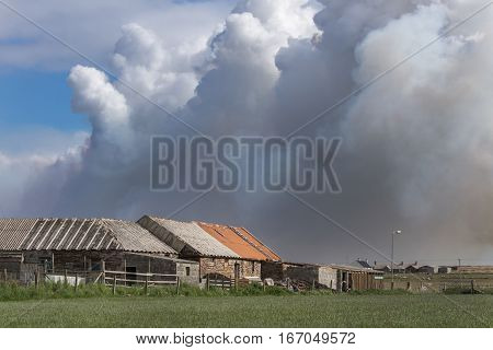 John O Groats Scotland - June 4 2012: Towering dark smoke clouds of large wildfire near John O Groats village threatens farm buildings. Green meadows gray and red buildings. One blue sky patch.