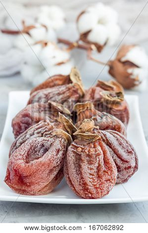 Several dried persimmon on white plate gray concrete background vertical