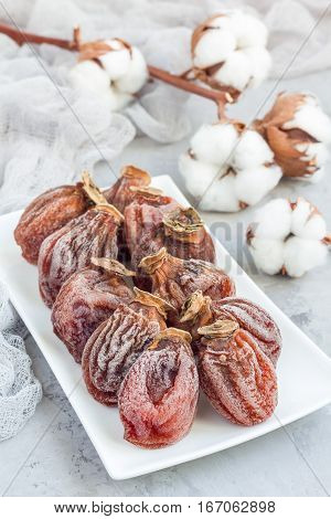 Several dried persimmon on white plate gray concrete background vertical