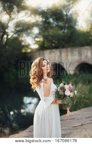 Beautiful bride with a big bouquet of different flowers posing on nature background