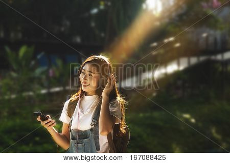 Asian hipster cute teen girl with backpack listening to the music with headphones lying on peak. Tourist traveler on background valley landscape view mock-up sunlight in trip in basque country