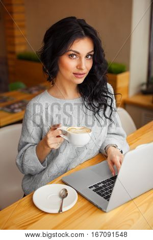 woman sitting at a laptop with a Cup of coffee and looking at the camera
