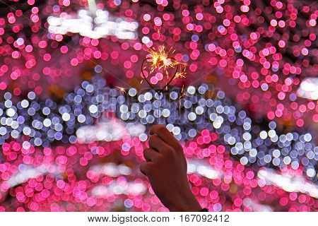 Hand holding sparkler in the shape of a heart in the background of colorful defocused lights