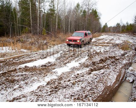 NIZHNY TAGIL. RUSSIA - JUNE 12 2013: Broken logging road in the heart of Siberia. Red offroad car overcomes winter thaw
