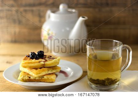Waffles with jam and green tea on a wooden background