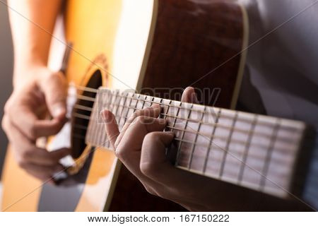 A man sitting and playing classic wooden guitar close up to chord tab fretboard.