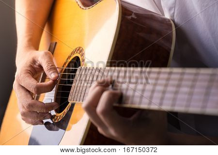 A man sitting and playing classic wooden guitar close up to chord tab fretboard.