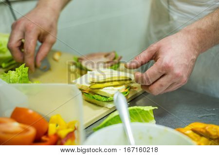 Cook making a sandwich with ham and pickles