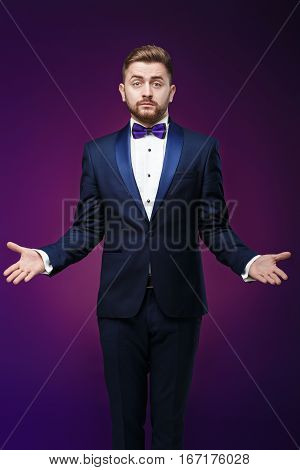 Handsome man in tuxedo and bow tie is surprised and throws his hands. compere in fashionable, festive clothing on dark background