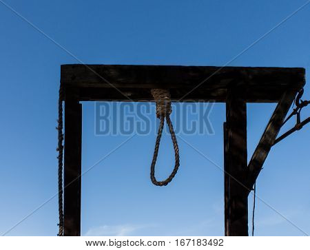 Wooden hangman's gallows with rope noose against blue sky