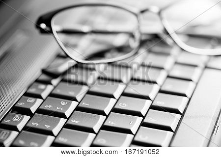Black laptop keyboard and glasses close up