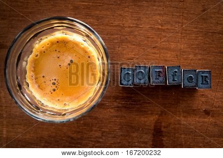 Flat lay of espresso in glass on timber background with rubber stamp lettering