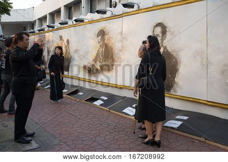 BANGKOK, THAILAND - DECEMBER 11, 2016: Thais in black mourning clothes are photographed at a wall with the image of the dead king Bhumibol Adulyadej. A fragment of funeral ceremonies in Bangkok