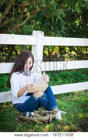 Pretty relaxed young asian woman reading a book at the lawn garen with sun shining vintage tone.
