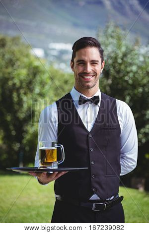 Handsome waiter holding a tray with a pint of beer outside