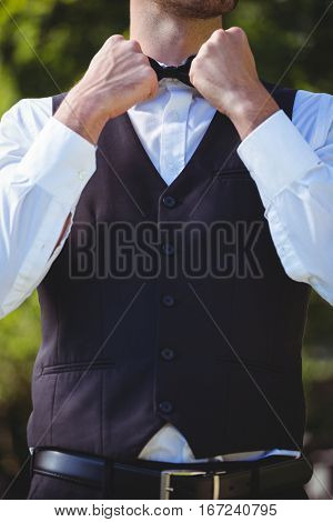 Handsome waiter reattaching his bow tie outside