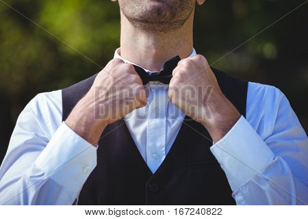 Handsome waiter reattaching his bow tie outside