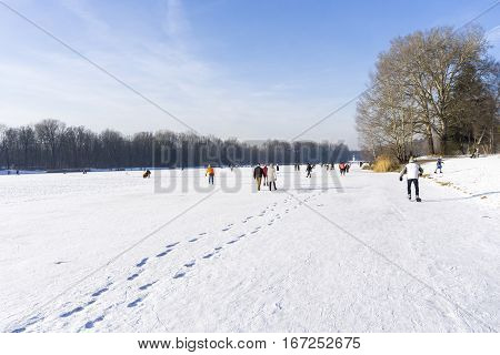 View on happy People on a frozen Lake.
Sporty People  with ice skates. Sunny Winter Day.
Kuhsee in Winter. 
Frozen Lake.
In Germany.
Augsburg. 
Winter Landscape in Bavaria.
