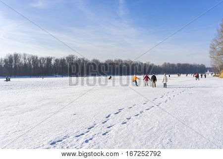 View on happy People on a frozen Lake.
Sporty People  with ice skates. Sunny Winter Day.
Kuhsee in Winter. Germany. Winter Landscape in Bavaria.