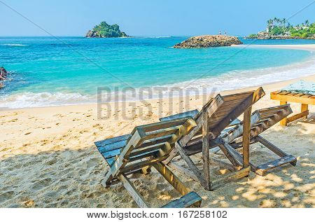 The wooden beach chairs stand in shade and are the best choice to relax with amazing views Midigama Sri Lanka.