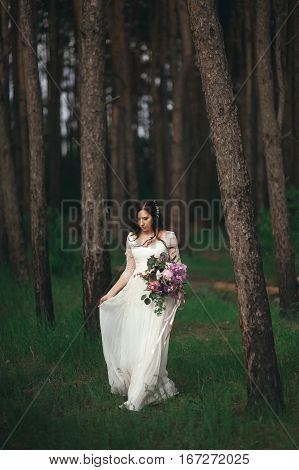 Beautiful bride in the forest with a large bouquet of different flowers. Boho style