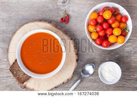 Tomato soup with dried herbs chilli tomoatoes and cream on the dark wooden table