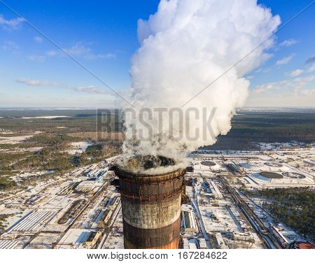 Heat electric station in winter. Aerial view. From above. Power station in a forest in sunny weather. Pipe with smoke close up