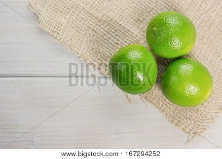 Three lime on the piece of cloth from a sacking on a wooden table.
