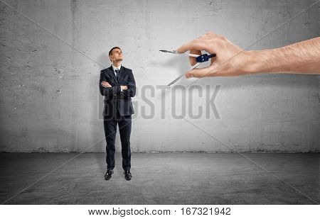 Small businessman on concrete background being measured by a giant hand with a metal compass. Business and success. Fitting in. Uniformity.