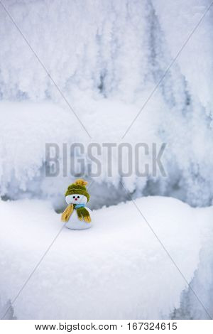 Fairytale character the snowman in hat and scarf is standing on fascinating fluffy snow near the hill and around there are frozen textured patterns.