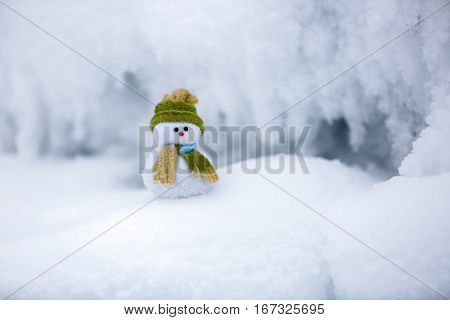 Snowman the Santa's assistant is standing in green hat wrapped with the scarf on nice textured snow on frosty winter morning.