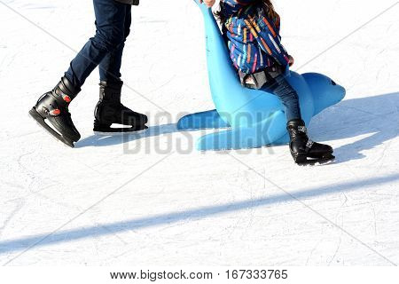 Family fun on outdoor ice rink, kid learning to skate with plastic seal as training aids