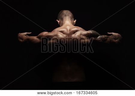 Unrecognizable man bodybuilder shows strong hands and neck muscles, athletic trapezius. Low key, studio shot on black background.