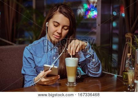 Music smartphone in female hand, on cafe interior background, injoy