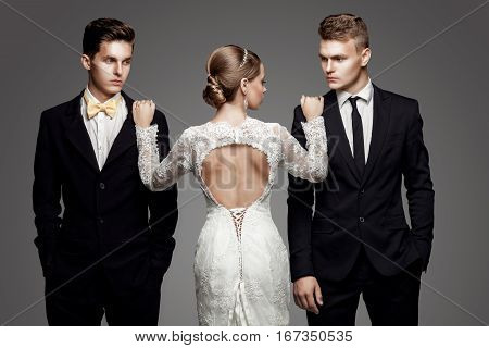 Two handsome men in suits and beautiful woman in white bridal dress. Studio, trendy, strict look
