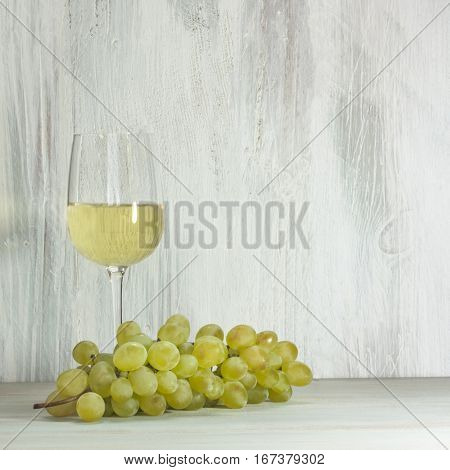 White grapes and a glass of white wine on a wooden background texture with copy space
